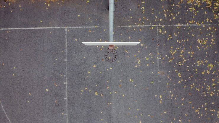 Ripresa con drone che si muove verso l'alto direttamente sopra un campo da basket in un parco pubblico.
