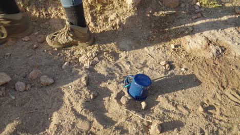 women hiker drops metal camping mug on desert hike with rocky landscape