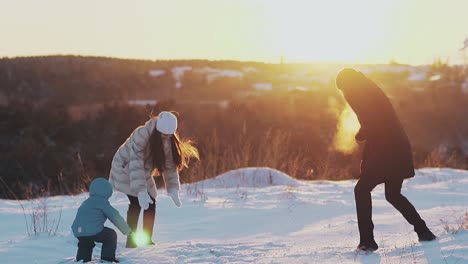 long haired lady and toddler son throw white snow to man