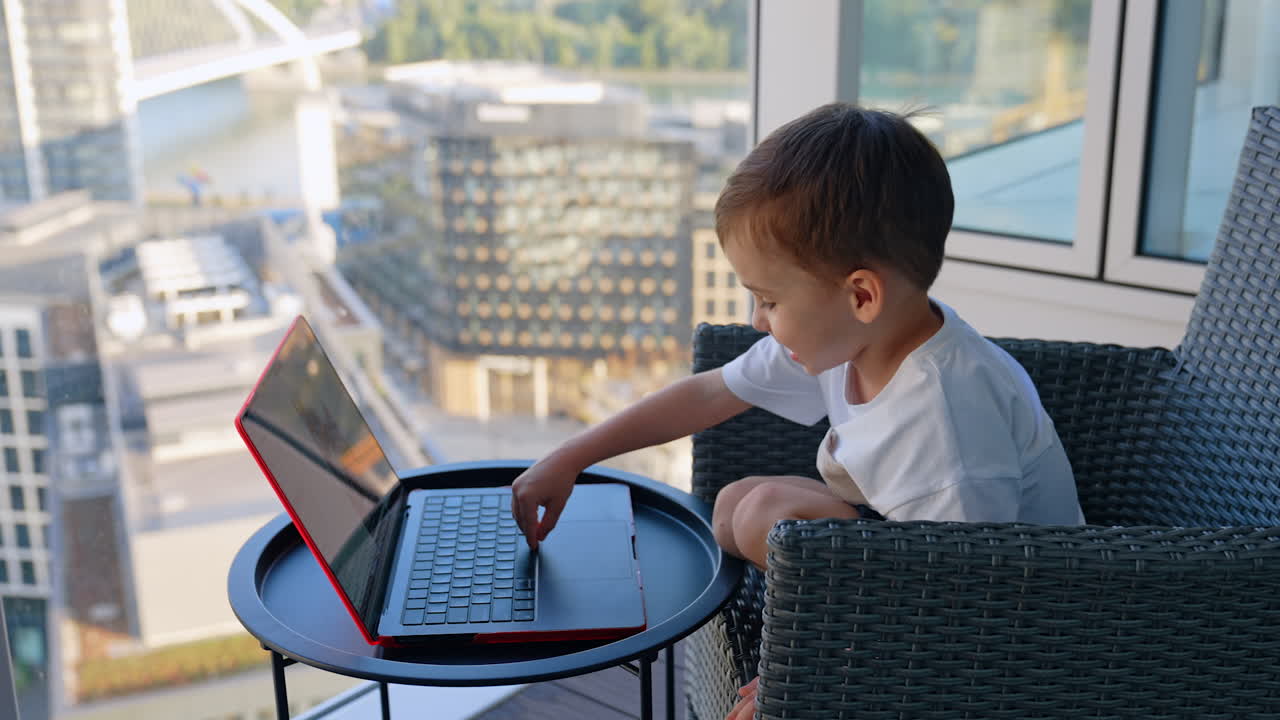 Child using laptop in city. Young child sits at a table using a laptop in a stylish urban apartment with a scenic city view