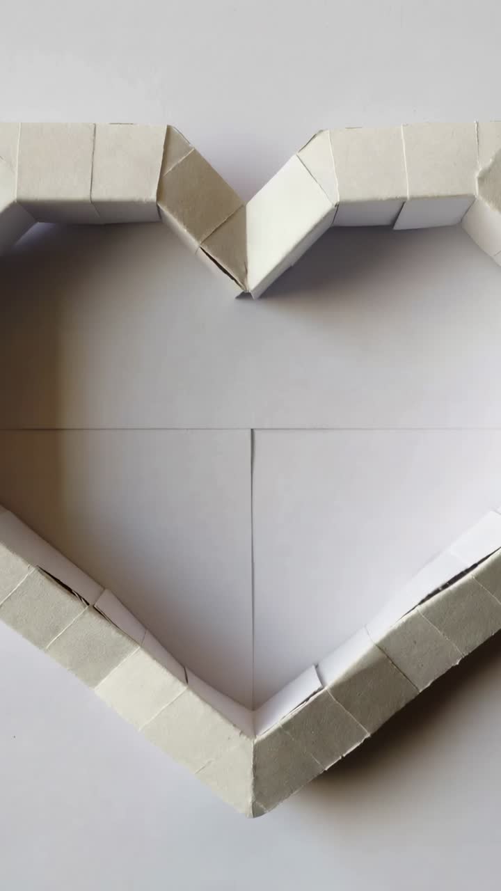 Video verticale: cuore di carta che rimane centrato su un foglio piegato, camera in movimento, ombre soffici