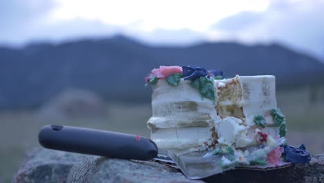 hübsche hochzeitstorte mit einem ausgeschnittenen stück, das auf einem felsbrocken in den bergen liegt