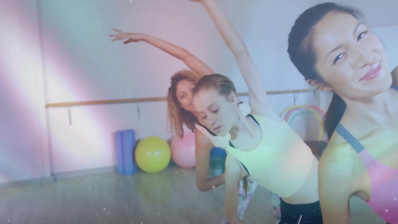 Fitness instruktor zvedá pravou paži a zahajuje boční protažení u baletní tyče, zatímco studenti napodobují pozici.