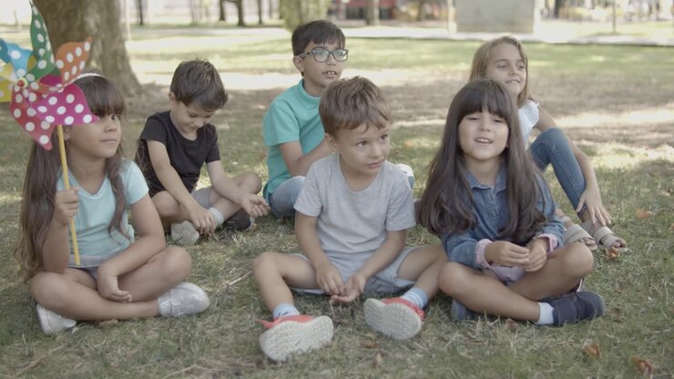 Bambini multietnici seduti sull'erba nel parco cittadino insieme.