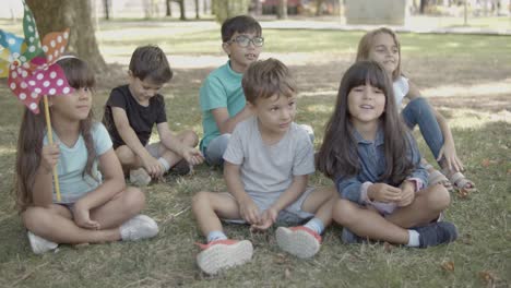 Multiethnic-kids-sitting-on-grass-in-city-park-together