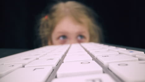 chica de ojos azules se esconde detrás de la mesa con el teclado de la computadora