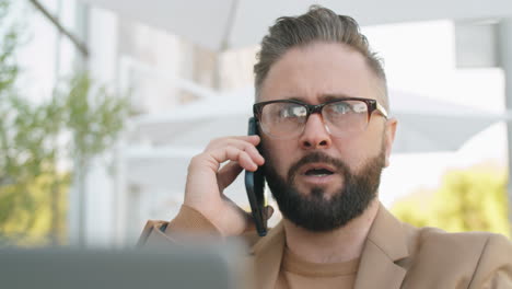 hombre de negocios caucásico hablando por teléfono y usando computadora portátil al aire libre
