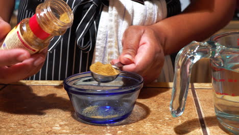 woman measuring tablespoon of cumin over glass blue bowl, close up