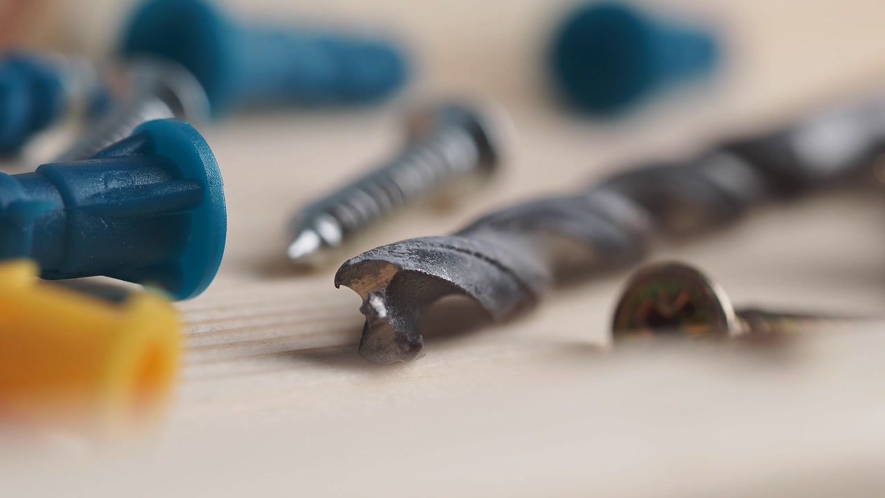 Close-up of a Drill Bit, Screws, and Wall Plugs on a Wooden Surface