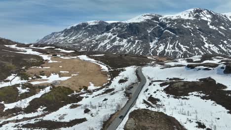 Car-crossing-Sognefjellet-mountain-pass-in-Norway-during-Summer---Boverdalen-towards-Lom-seen-in-background---Aerial