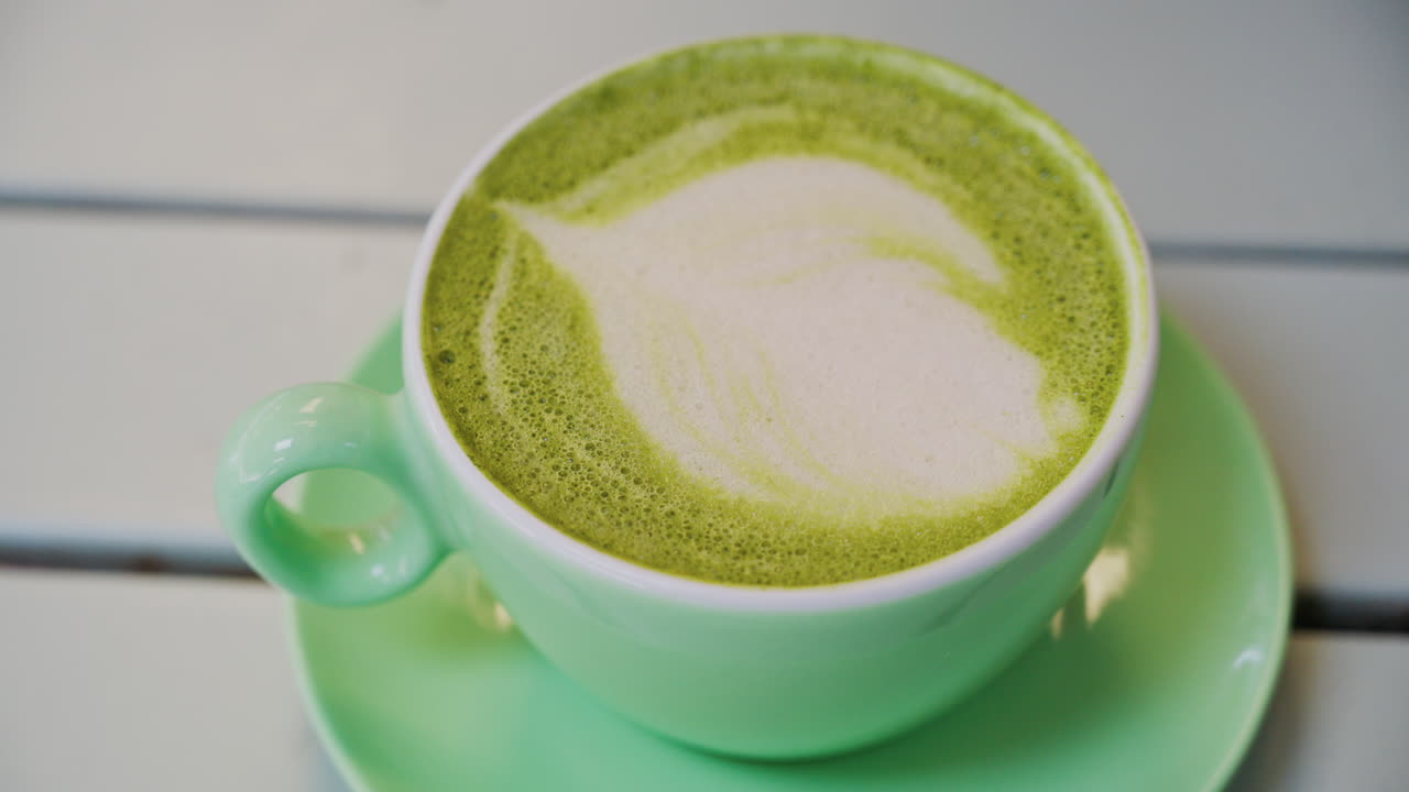 Close up of a matcha latte in a green cup on a terrace table