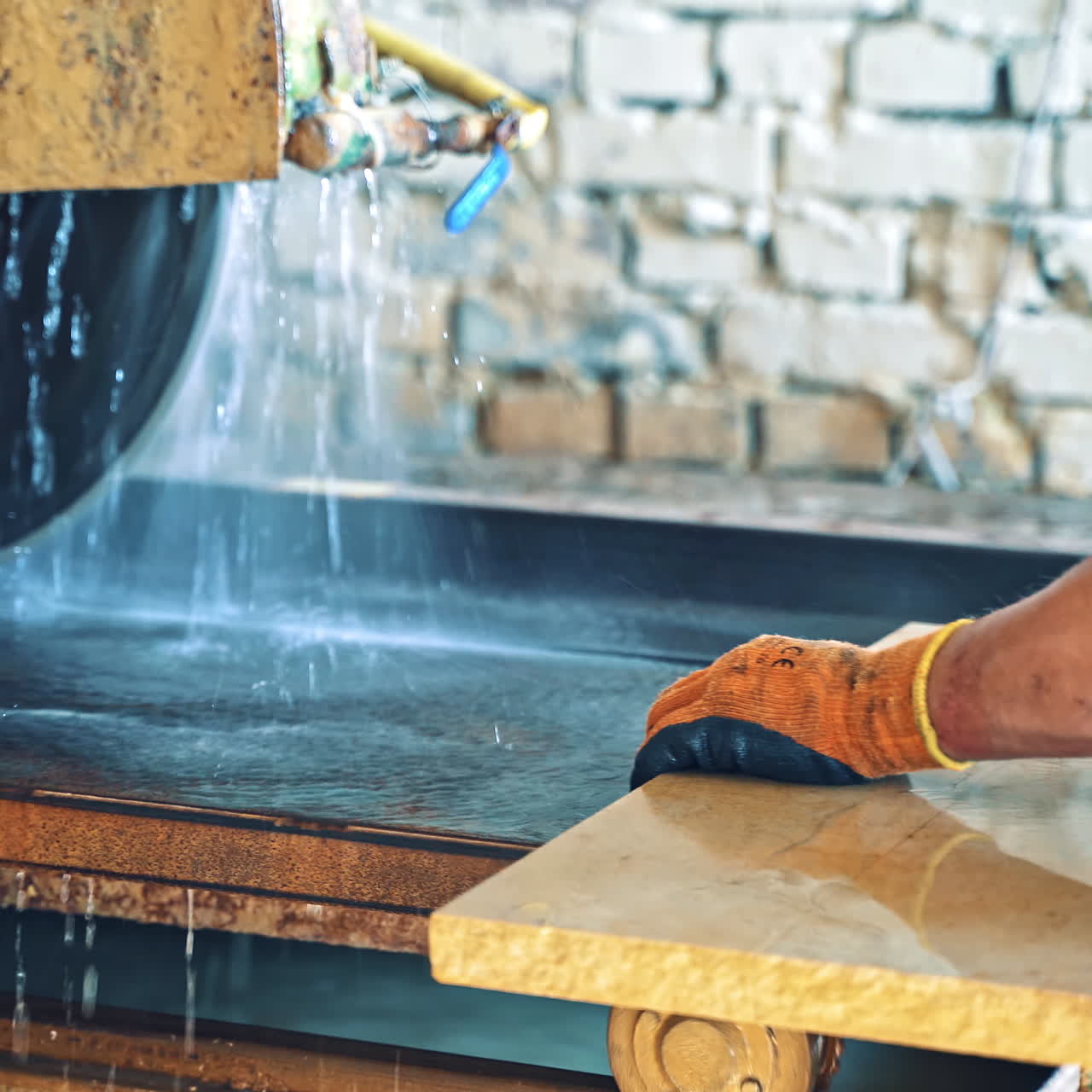 Male's hands in gloves holding stone slab close to the automated machine. Automated circular saw cuts the stone slab at industrial factory. Worker controls the electric cutter machine.