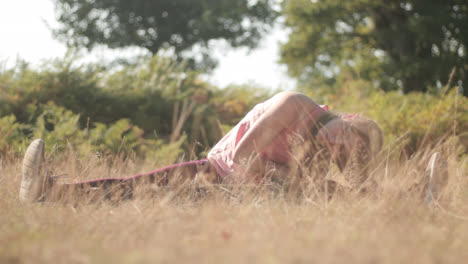 A-woman-is-sitting-in-the-dry-grass-touching-her-toe-with-her-hand-for-stretching-her-back-in-the-park-outdoor