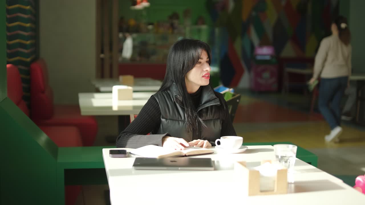 검은색 의상을 입은 전문적인 여성 관리자가 사무실을 걸어다니며 동료들과 상호 작용하며 문서와 노트북을 들고 리더십과 전문성을 보여주고 있습니다.