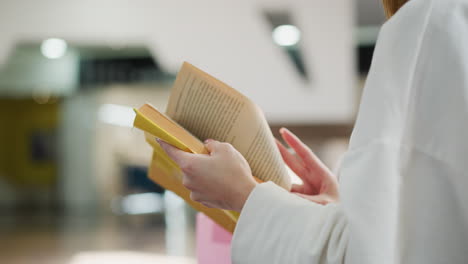 close-up of hands flipping through a yellow-covered book, showcasing elegant gestures and delicate details, set in a softly lit indoor environment with a blurred modern background