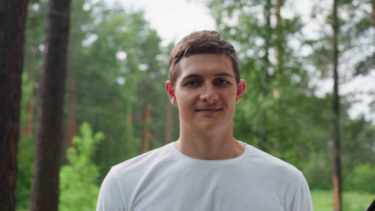Retrato de un niño enérgico que se quita la cesta de pícnic del hombro con una sonrisa alegre mientras está de pie junto al coche en un bosque verde, disfrutando del aire fresco, la luz del sol y un paisaje veraniego apacible.