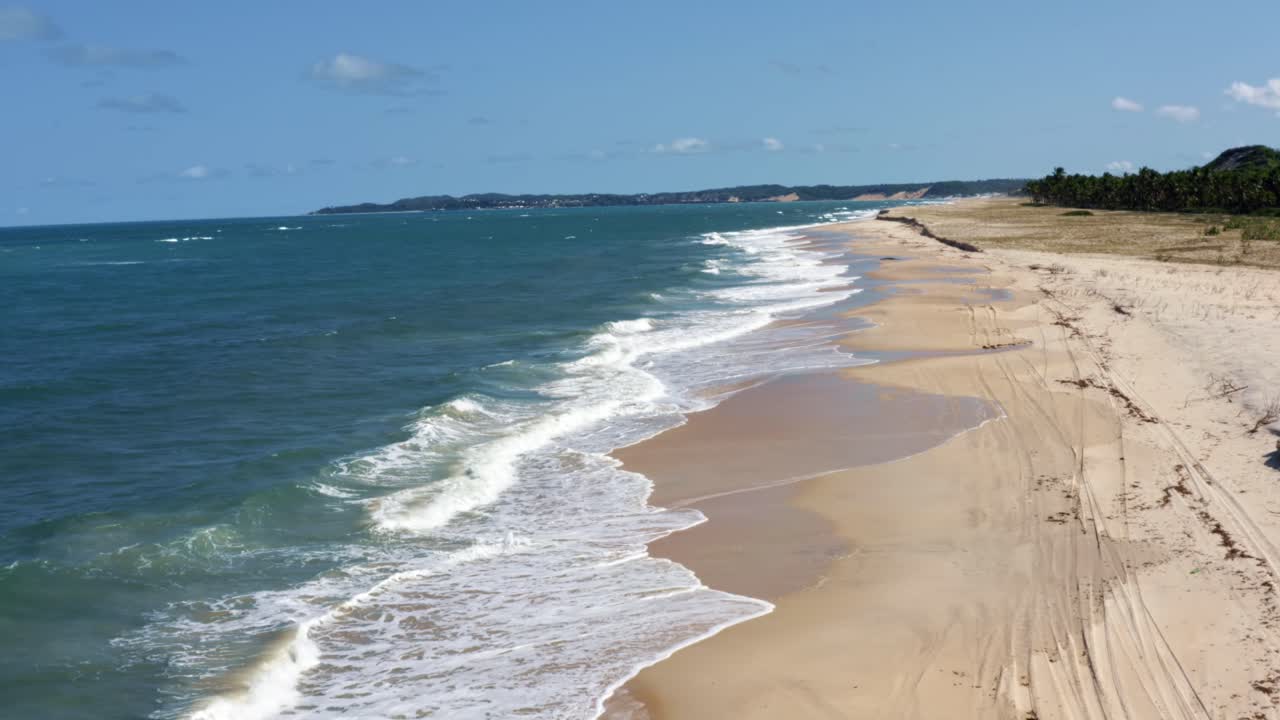 Dolly out aerial drone shot of the tropical coastline of Rio Grande do Norte, Brazil with a white untouched beach, small calm waves, and palm trees in between Baia Formosa and Barra de Cunha?