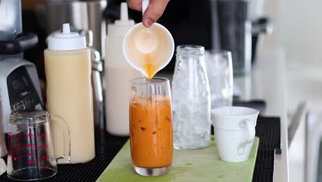 vertiendo batido de zanahoria en un vaso con hielo