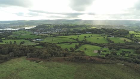 sunbeams moving across overcast british agricultural rural village countryside morning aerial view right dolly