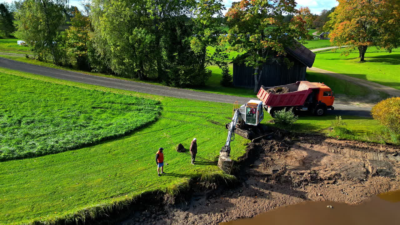 Excavator and truck removing earth along the banks of a pond in a rural landscape
