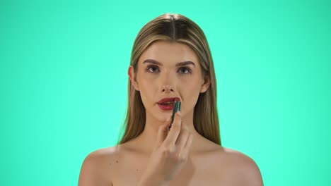 disparo en cámara lenta de una joven atractiva mujer rubia caucásica mientras aplica lápiz labial rojo en sus labios para prepararse para la noche o la cita mientras se ve sexy a la cámara