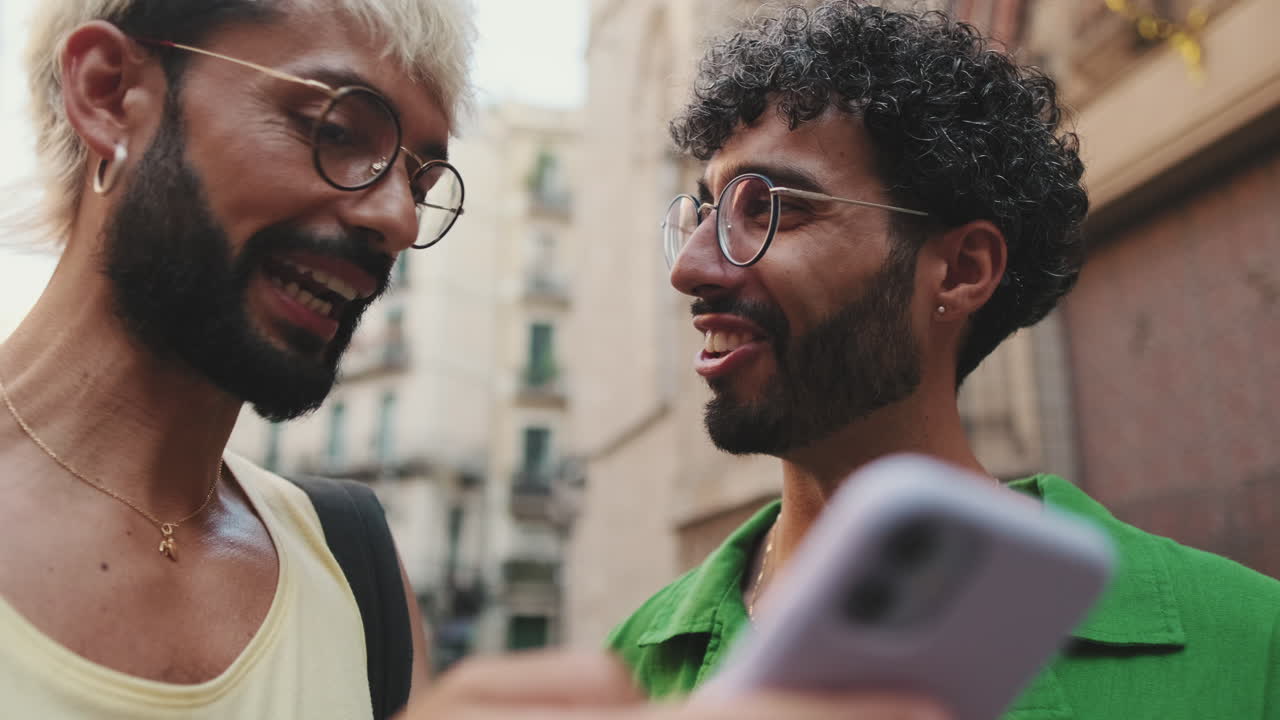 Two Young Men Smiling and Talking While Looking at Smartphone