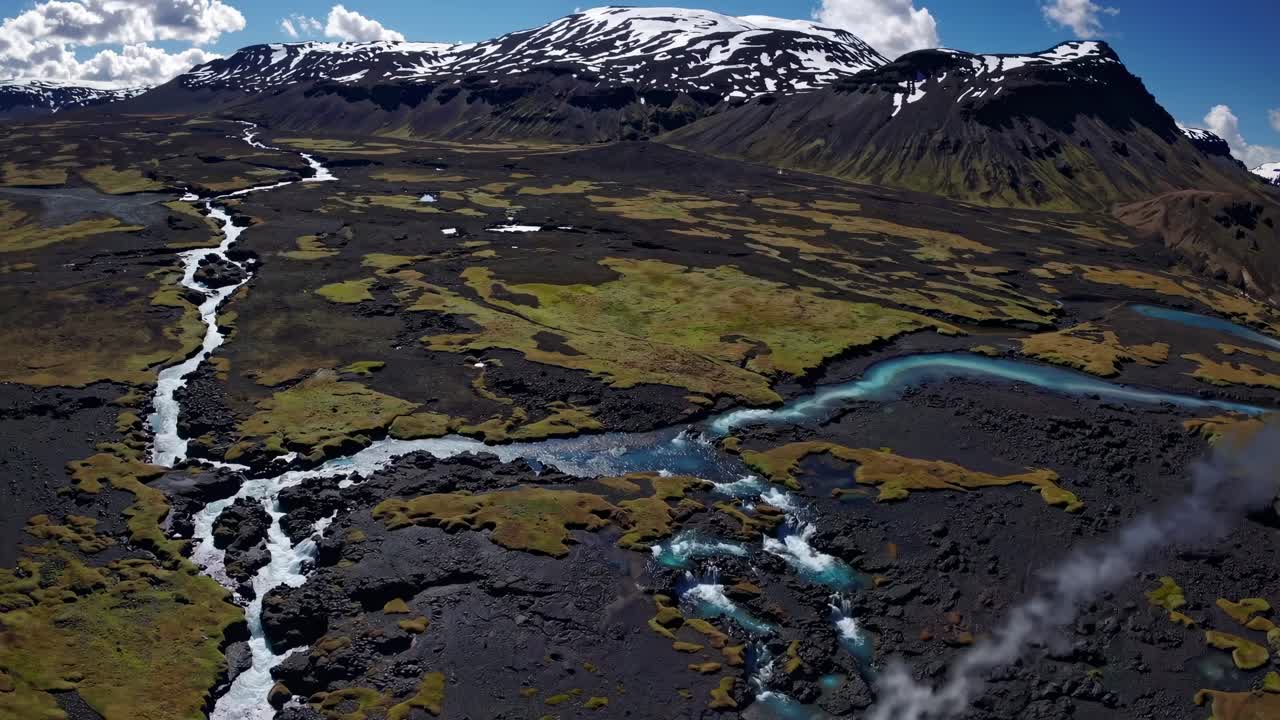 Aerial video captures a vast, rugged landscape with winding rivers and snow-capped mountains