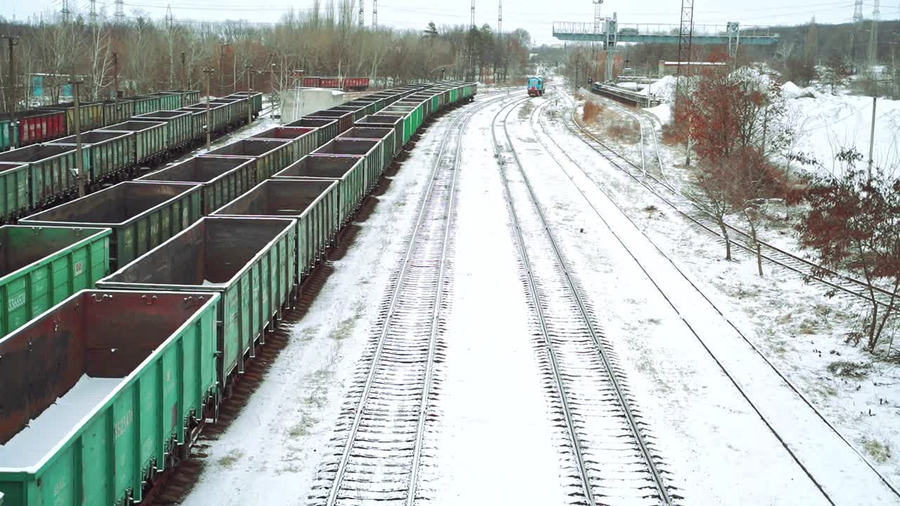 Aerial view on a huge number of iron containers of different colors located at the final station on the background of a freight train, which is moving in their direction. Close-up.
