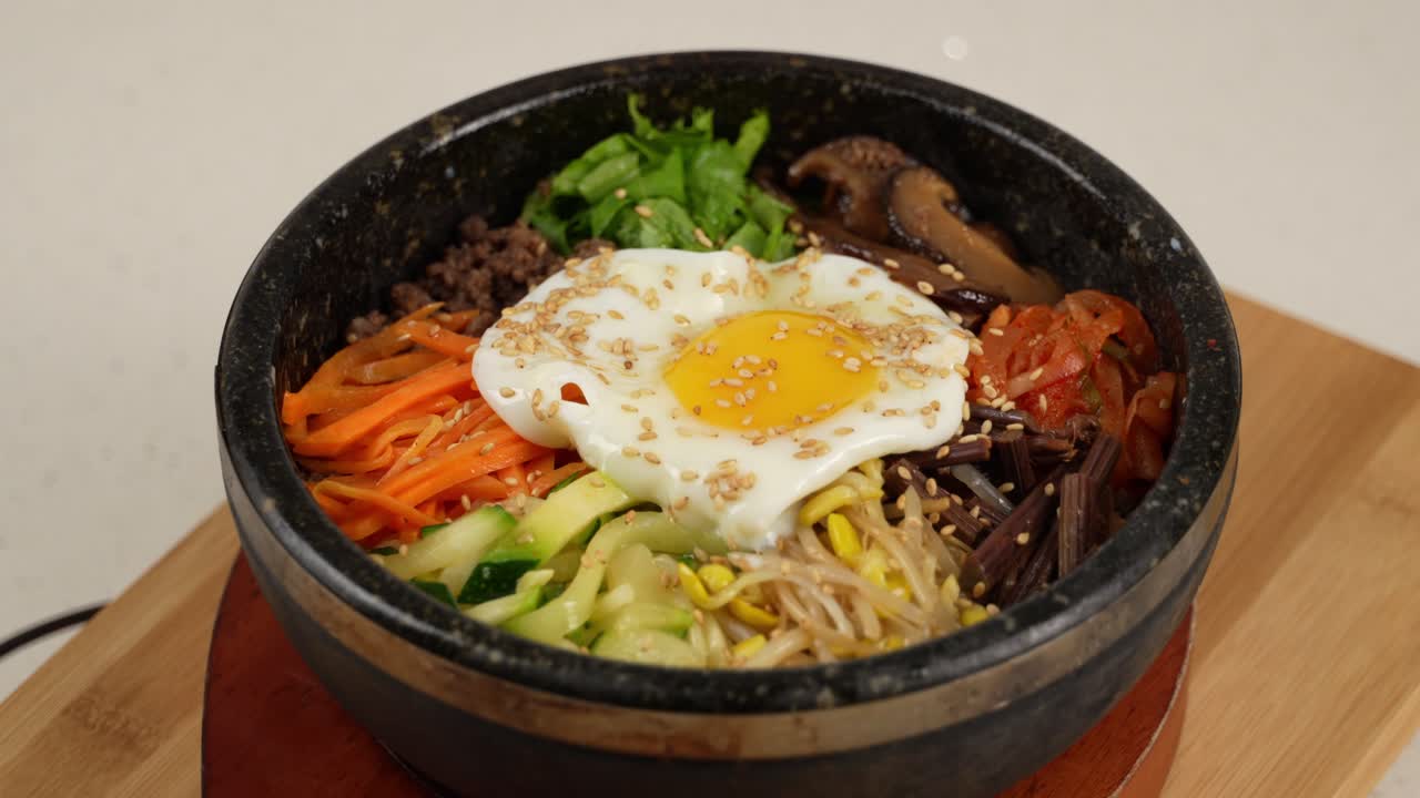 Warm stone bowl with rice, seasoned vegetables, beef, and egg, mixed with spicy sauce. 뜨거운 돌솥에 밥, 나물, 고기, 계란이 어우러진 매콤한 한 그릇.