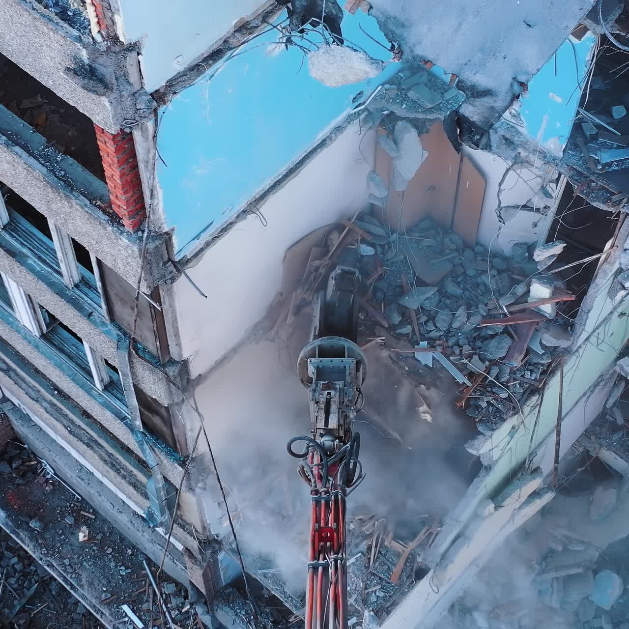 Excavator grabber tears off the pieces of destroyed building. Heavy machinery working at destruction site. View from above