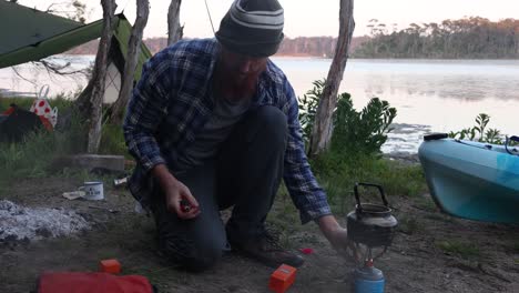 a man boils water on a gas stove at a remote camp on an australian lake