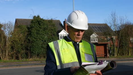 an architect senior building construction manager on a residential street with traffic and houses looking at paperwork inspecting the building