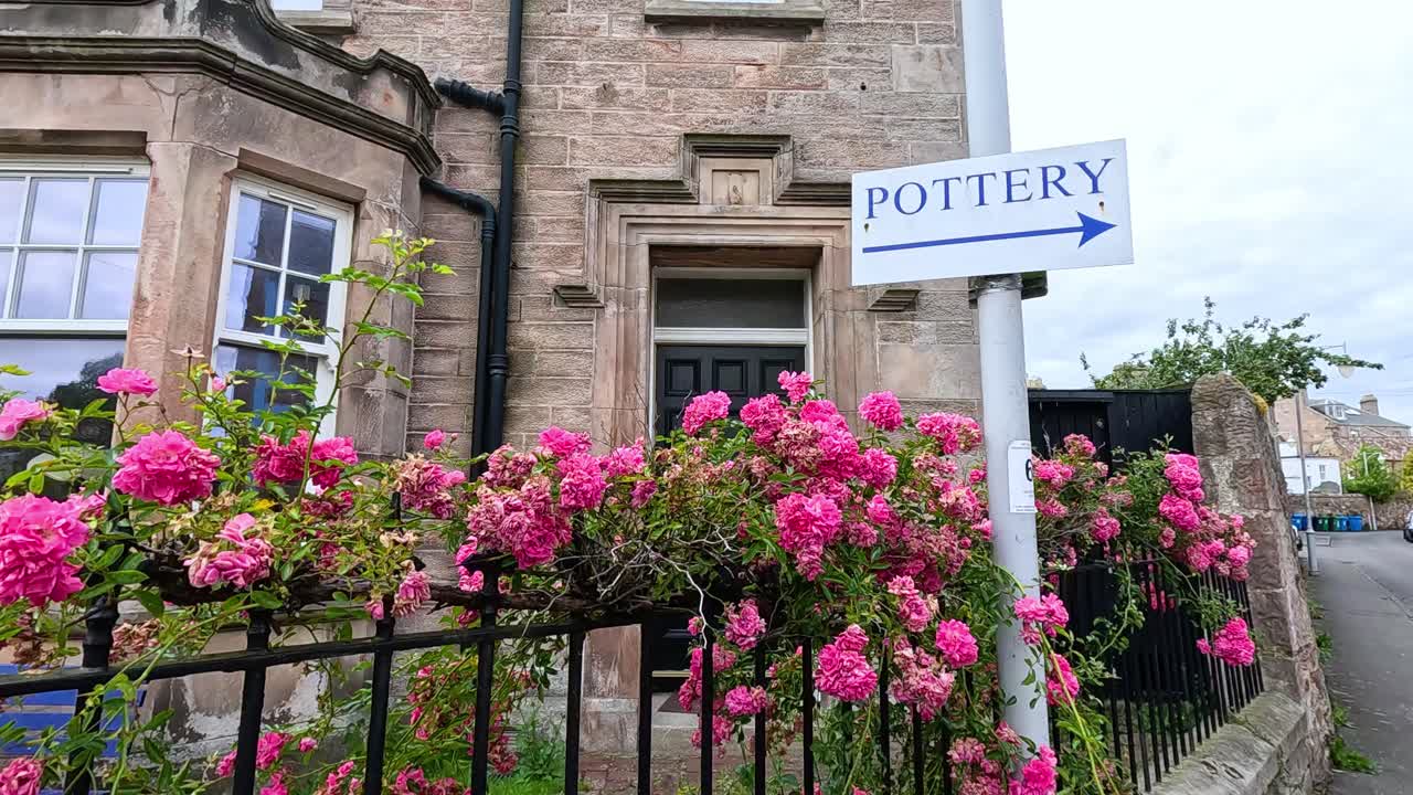 꽃이 피는 분홍색 장미로 둘러싸인 도자기 가게 표지판