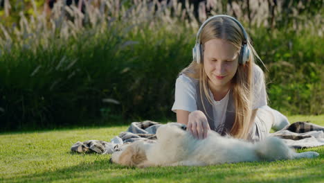 una adolescente juega con un cachorro, se acuesta en el césped, escucha música con auriculares