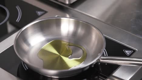 a frying pan on the stove and a hand in black glove pours some oil from the bottle, then adds some garlic and a leaf of spinach