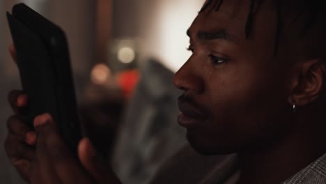 Young-black-male-using-watches-something-on-his-tablet-device-while-sat-on-the-sofa