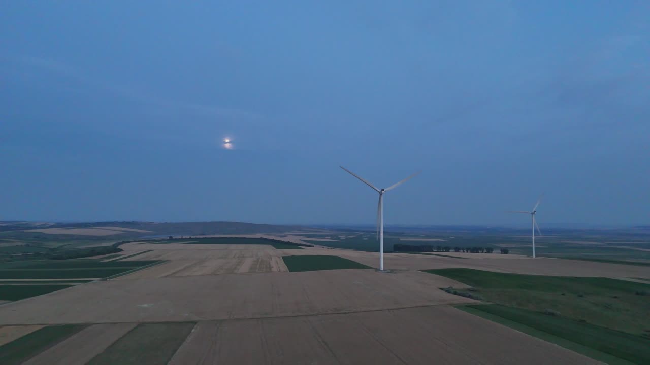 Drone video of wind turbines near Ruginoasa, Iași, Romania, with the moon glowing against a twilight sky