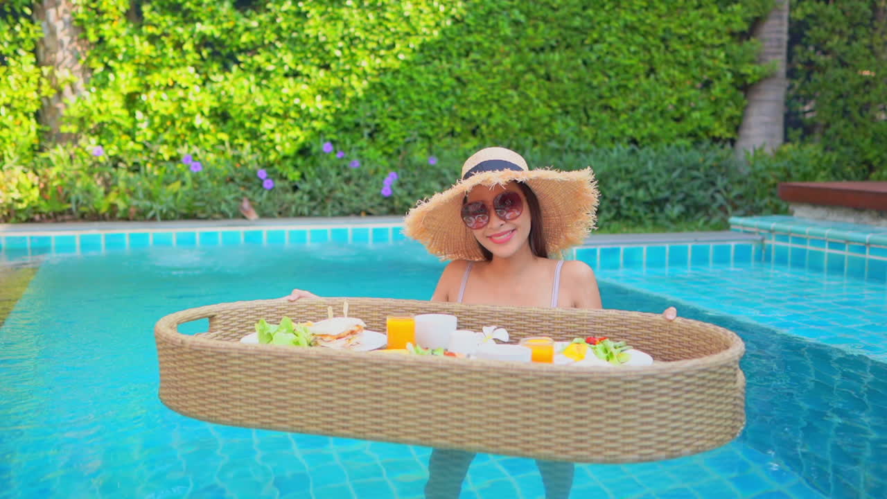 Young Asian woman stands in shallow swimming pool with floating food tray