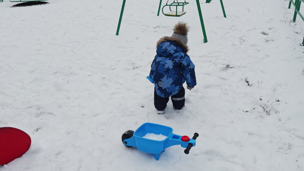 Little kid wearing warm coat, pants and cap holding a shovel. Toddler boy digging the snow outdoors.