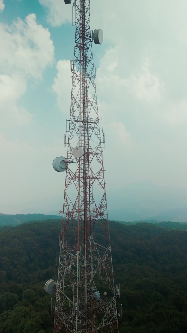 Torre di telecomunicazione con antenne contro un cielo nuvoloso sopra una foresta.