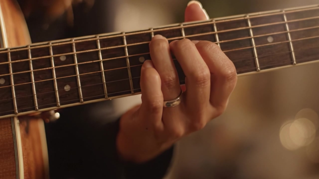 Primo piano di una mano che suona la chitarra acustica: un momento di espressione musicale e intimità catturato in due fotogrammi