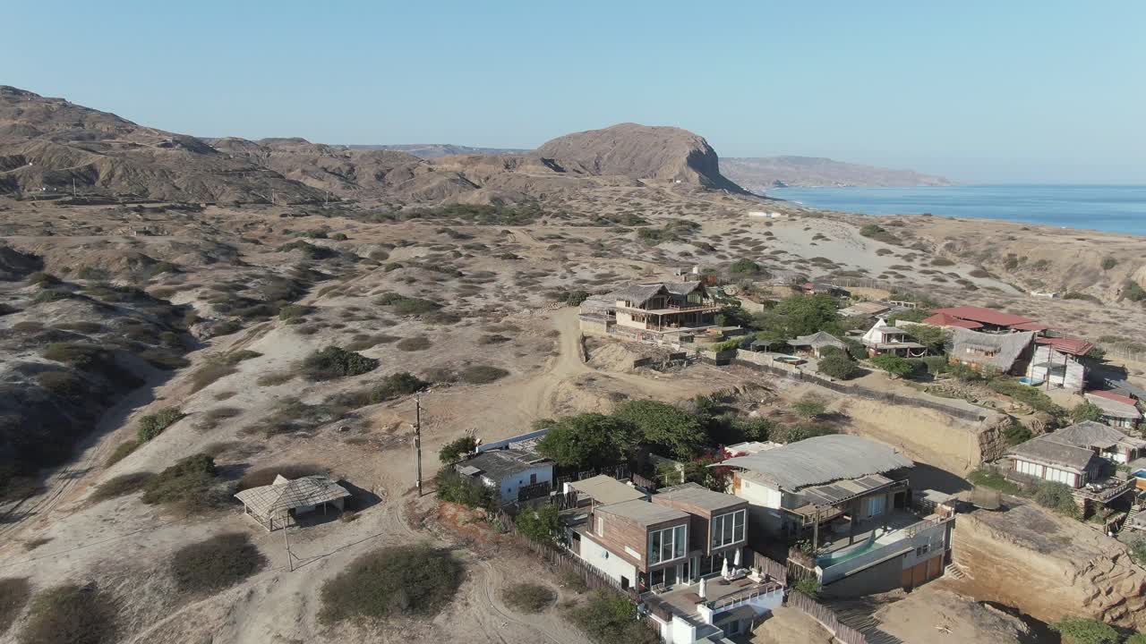 Denize sırtını dönmüş bir şekilde sahilden uzaklaşan kameranın, Peru, Piura'daki Los Organos sahil şeridinin havadan drone çekim görüntüsü. Punta Veleros'tan kum tepeleri ve evler