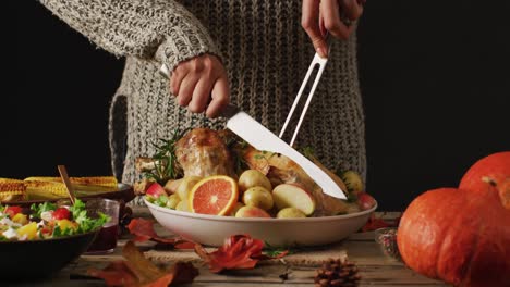 video of midsection of caucasian woman cutting roasted turkey on table with autumn decoration