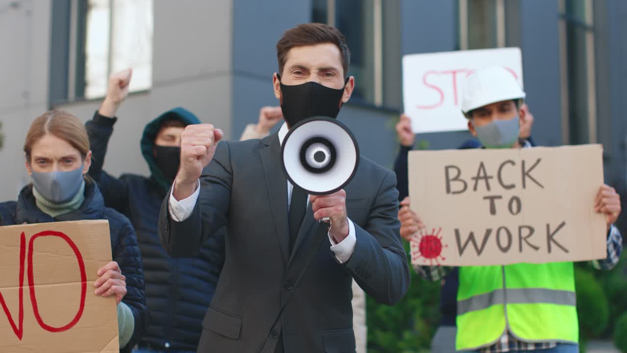 코비드 19에 대한 항의에서 확성기에서 소리를 지르고 카메라를 바라보는 보호 마스크를 쓴 백인 남자