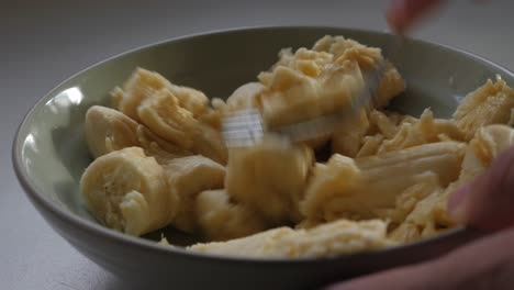 person mashing chopped banana in small bowl with a metal fork on benchtop