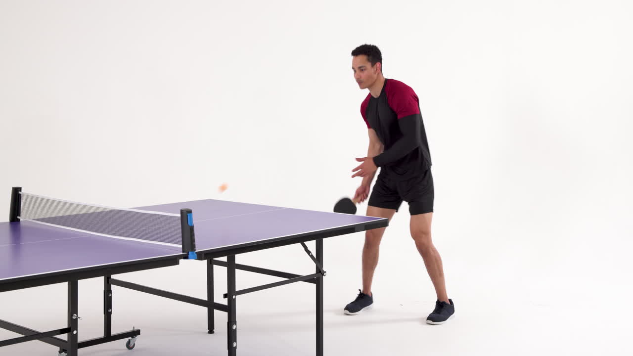Playing table tennis, man hitting ball with paddle in studio setting