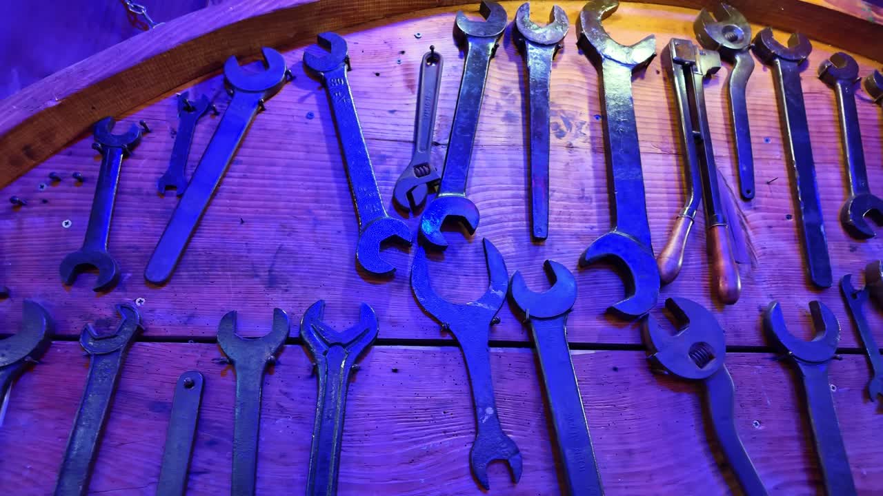 Vintage wrenches and spanners of various sizes hanging on a wooden wall, illuminated by a blue and purple light for decoration