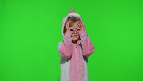 Child-girl-in-unicorn-pajamas-fooling-around,-looks-through-her-hands-as-if-through-binoculars