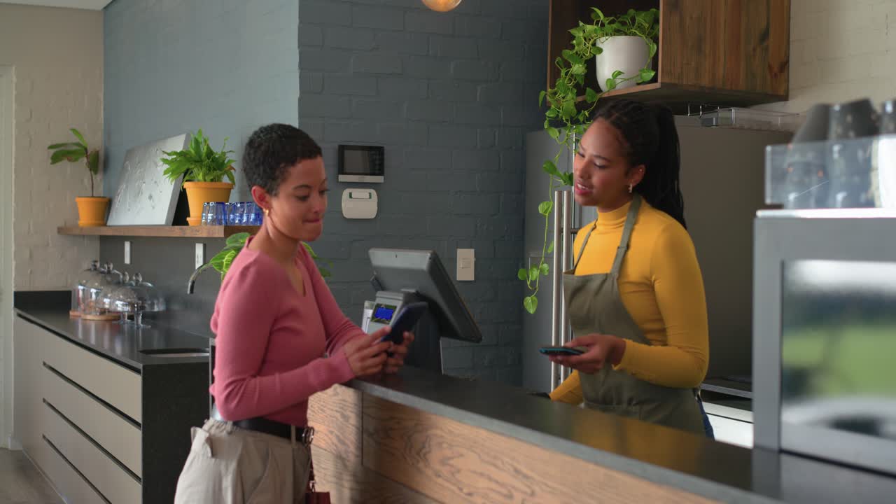Customer entering and scanning smartphone for payment on reader, cashier tapping till at counter