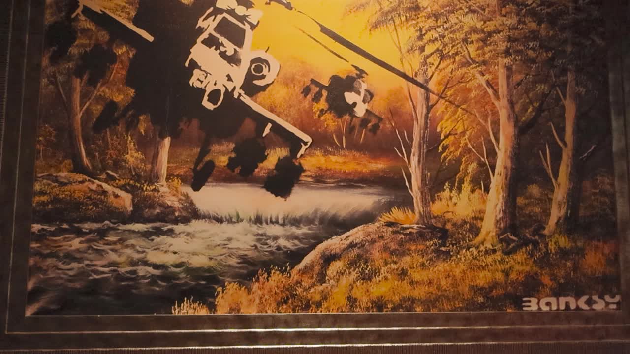 Oil painting made by Banksy that has two black hawk helicopters on it done in stencil art. Artwork is called Flying chopper and shows choppers flying through forest with a river flowing underneath.